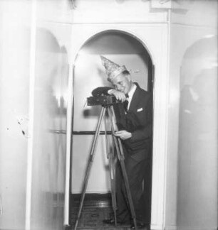 Bordleben. Der Bordfotograf Franz Grasser mit Plattenkamera auf Stativ und Karnevalshut