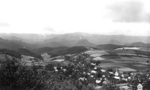 Saupsdorf (Sebnitz-Saupsdorf). Ortsteilansicht mit Dorfkirche und Waldhufen. Blick vom Wachberg nach Südsüdwest gegen Hintere Sächsische Schweiz mit Raumberg und Winterbergmassiv bei Wolkentreiben
