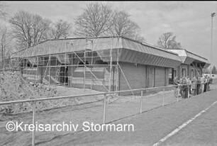 Mehrzweckhalle: Ringstraße: Richtfest: hinten Rohbau mit Gerüst: rechts Gäste: links Sandhaufen und Baumaterial: im Vordergrund Fußballfeld: im Hintergrund Bäume: 12. April 1985