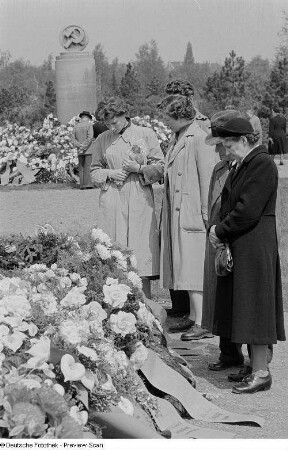 Personengruppe vor dem mit Blumen und Kränzen geschmückten Sowjetischen Ehrenmal auf dem Ostfriedhof