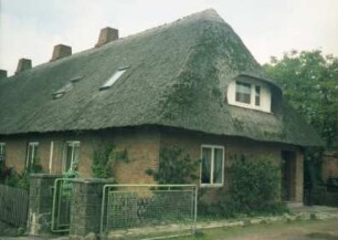 Neufresenburg: ehemalige Gutsarbeiterkate: traufständige Mehrfamilienkate aus Backstein mit Reetdach: Straßenfront, Teilansicht: Giebelseite mit Eingangstür