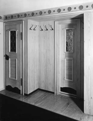 Einbauschrank und Zimmertür im Landhausstil (um 1950), vermutlich in einer Gaststätte mit geschnitzter Wandbordüre (wahrscheinlich im Allgäu). Ansicht mit Garderobenhaken