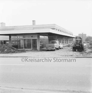 Industriestraße: Firmengebäude im Bau: Rohbau mit Fenstern: davor unbefestigtes Gelände mit Erdhaufen und Baumaterial: rechts Kleintransporter, Pkw und Bagger: im Hintergrund Wohnblock am Stoltenrieden: 20. Juni 1971