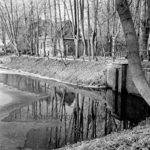 Schlossmühle: Mühlenredder, Bäume, rechts Brücke des Mühlenredder über dem Abfluss des Schlossgrabens: davor äußerer Schlossgraben mit Eisdecke: Rauhreif: im Winter