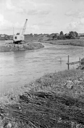 Trave: Flussregulierung: vorn Reisigbündel: hinten links Bagger, Loren und Baumaterial: hinten rechts und links des Ufers Wiesen und Büsche: dahinter Häuser von Sehmsdorf zwischen Bäumen