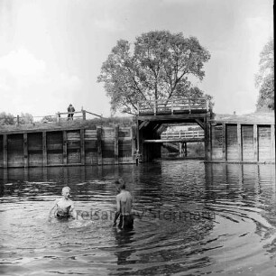 Alster: Wulksfelder Schleuse mit Schleusenbrücke: vorn links zwei Jungen im Wasser: in der Mitte rechts und links Holzverschalungen: hinten links am Geländer Mann: hinten Mitte Baum