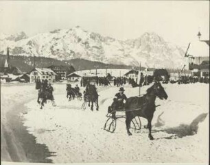Winter im Hochgebirge. Auf der verschneiten Dorfstraße findet eine Wettfahrt der Pferdeschlitten statt