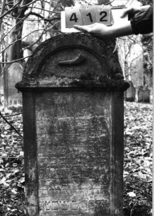 Grabstein 412 (Index: 99752676) Material: Sandstein Zustand: stark verwitt. mit fast völl. Textverlust Maße HxBxT: 107x52x15 cm Beschreibung: Stele, Abdeckplatte mit Rundbogenaufsatz, rechteckiges Schriftfeld eingetieft Symbolik: Schofar: Grabstein 412