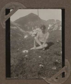 Heinrich Zimmer in Badehose auf einer Wiese vor Bergen sitzend