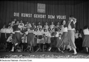 Tanzende Paare, im Hintergrund Chor und Orchester beim Kreisausscheid für Volkskunst