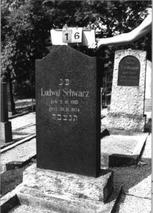 Grabstein 16 (Index: 99793200) Material: schwarzer Granit Zustand: gut Maße HxBxT: 118x49x14 cm Beschreibung: Stele, horizontal eingezogener Giebelabschluß, getreppter Sockel, Grabeinfassung: Grabstein 16