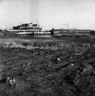 Schule am Masurenweg [Dörfergemeinschaftsschule, Grund- und Hauptschule]: Rohbau: dahinter Baukräne: vorn Erdhaufen und Wiese: 11.11.1972