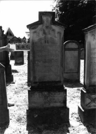 Grabstein 186 (Index: 99797620) Material: Sandstein, weiß Zustand: leicht verwittert Maße HxBxT: 200x67x20 cm Beschreibung: Stele, Giebel rechteckig erhöht, getreppter Sockel Symbolik: Blüte, Rundbogenfries: Grabstein 186