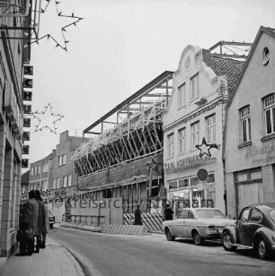 Firma Carl Hoffmann: Hindenburgstraße: Elektrohandel: Neubau: Aufbau des Stahlgerüsts und Verkleidung: davor Bauzaun: hinten links Wohn- und Geschäftshaus des Haushaltswarengeschäfts Otto Möller: vorn links Fußgänger: rechts altes Wohn- und Geschäftshauses Carl Hoffmann: davor zwei parkende Pkws