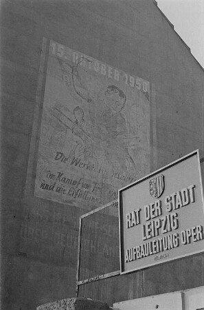 Blick auf eine Häuserfassade am Augustusplatz (damals Karl-Marx-Platz) in Leipzig mit einer Losung anlässlich der ersten Volkskammerwahlen am 15. Oktober 1950, im Vordergrund ein Schild mit der Aufschrift "Rat der Stadt Leipzig, Aufbauleitung Oper"