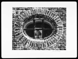 Holland. Ovales, vergittertes Fenster in Klinkermauerwerk