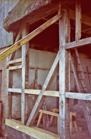 Beimoorweg (47): Fachwerkhaus mit Reetdach: bei Renovierung: Teilansicht: Gefache Außenwand ohne Ausmauerung, oben Stützbalken: Blick in Innenraum, Innenwand, Holzleiter, Baumaterial: hinten links Außenmauer, oben Verbretterung