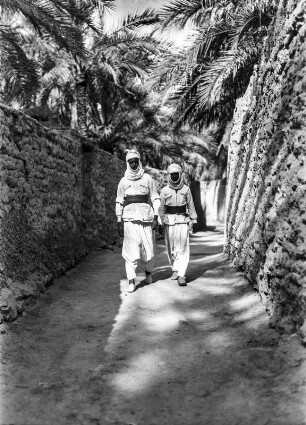 Männer in Ghadames : Zwei Männer gehen durch eine von Palmen beschattete Straße in Ghadames
