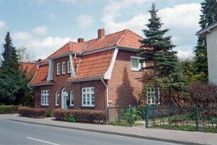 Lübecker Straße 14: traufständiges Wohnhaus aus Backstein mit Krüppelmansarddach: Straßenfront: Eingangstür, beiderseits Rundbogenfenster, Sprossenfenster, mittig Zwerchgiebel: Giebelseite: Vorgartenhecke: rechts Vorgarten, Zaun