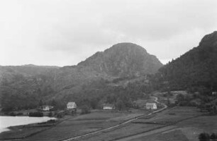 Landschaft : Berge am Rand eines Gewässers. Davor eine Siedlung.