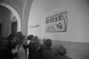 Dekorative Ausgestaltung der Klassenräume und Schulflure in der Einheitsschule Baumschulenweg und Oberschule Niederschöneweide in Vorbereitung des Deutschlandtreffens der Jugend für Frieden und Völkerfreundschaft zu Pfingsten 1950 : Schüler vor einem Plakat zum Deutschlandtreffen an einer Wand im Hausflur einer Schule