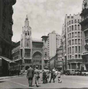 Barcelona. Spanien. Hochäuser an einem Platz. Passanten überqueren diesen