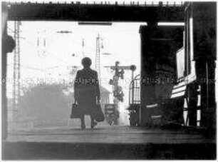 Alte Frau mit Tasche im Gegenlicht, sie läuft auf einem Bahnsteig (Altersgruppe 14-17)
