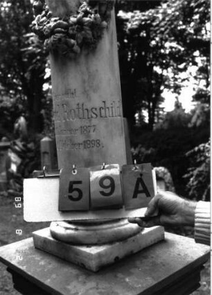 Grabstein 59 (Index: 100101498) Material: Säule weißer Marmor, Postament Sandstein Zustand: deutsche Sockelinschrift verwittert mit Textverlust Maße HxBxT: 200x56x48 cm Beschreibung: postamentierte abgebrochene Säule, Schriftplatte mit ausgezogenen Ecken Symbolik: Blütenkranz um Säule: Grabstein 59A