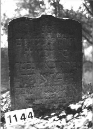 Grabstein 1144 (Index: 99899853) Material: Sandstein Zustand: vor allem unten stark verwittert, etwas eingesunken Maße HxBxT: 82x44x9 cm Beschreibung: Stele mit Schulterbogenabschluss, im Bogenfeld Blumen, etwas eingesunken Symbolik: Blumen: Grabstein 1144