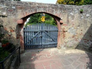 Friedhof-Ansicht im Nordwesten mit Kirchhofmauer sowie Torbogen mit erhaltenen steinernen Torangeln am oberen Gewände-Wehrgang mit Steinbrüstung sowie Toranlage im 18 Jh abgetragen