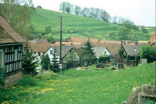 Blick vom Friedhof über das Dorf nach W, Grabsteine, Dächer, hinten Ackerterrassen