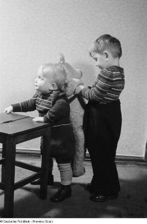 Zwei Kinder, eines spielt mit einem Teddybären