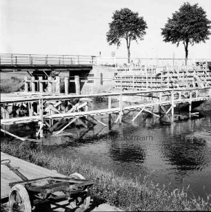 Trave: Brückenneubau: rechts Holzgerüstbau für neue Brücke: vorn Notsteg: im Hintergrund alte Holzbrücke und zwei Bäume