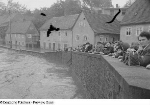 Menschen an einer Mauer, auf das Hochwasser schauend