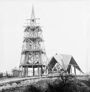 Rethwischdorf: Christuskirche: Rohbau: Außenansicht von Westen: Faltdachstuhl und eingerüsteter Glockenturm: darauf Dachdecker: darunter Baubude, Baufahrzeug und Baumaterial