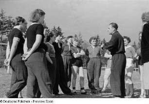 Porträt eines Trainers und mehreren Sportlerinnen auf dem Sportplatz der Sportschule