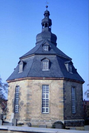 Blick auf den Chor der Kirche; im Vordergrund Friedhofsmauer und Grabsteine