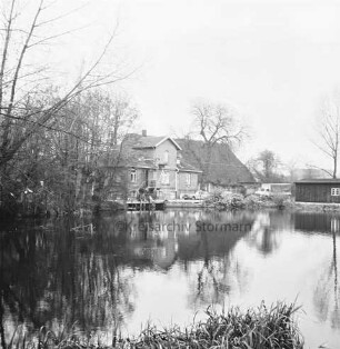 Mühlenteich: vorn links Sträucher: hinten Mitte Mühle: davor Pkws und Lkw sowie Personen: rechts Schuppen
