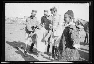 "Maurenstadt" neben dem Lager von Nador (Marokko): 3 Offiziere [des spanischen 8. Kavallerie-Regiments "Lusitania"] in hellgestreiften Uniformhosen, hellgestreifter und dunkler Uniformjacke und mit niedrigen, runden Feldmützen und 2 einheimische Jungen beim Schabernack [Eröffnung der Bahnstrecke Nador-Zeluan (Selouane, Marokko]