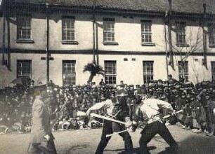 Nagasaki. Zwei japanische Soldaten beim Fechtkampf vor Zuschauern. Blick gegen eine Kaserne