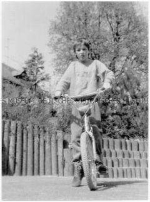 Junge mit Fahrrad auf einem Spielplatz (Altersgruppe bis 14)