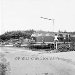 Rohlfshagen: Bahnübergang an der Kreisstraße Richtung Rümpel: geschlossene Schranke und Andreaskreuz: rechts durchfahrende Lokomotive