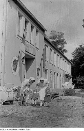 Pflegerinnen mit Kindern vor dem Heimgebäude