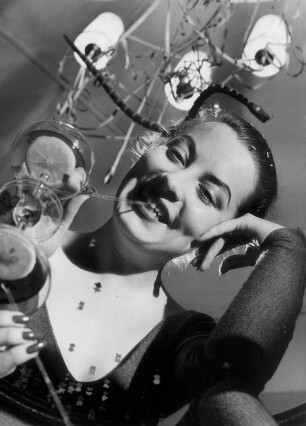 Die Frau des Fotografen zu Silvester 1954. Sie trinkt genießerisch einen Cocktail. Fotografiert durch einen Glastisch.