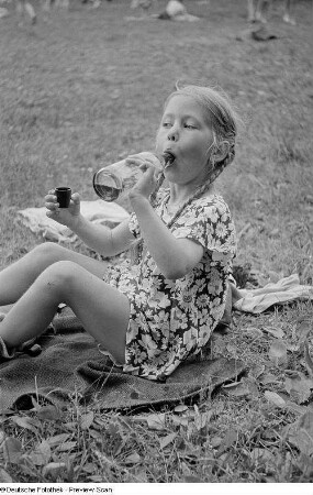Mädchen beim Trinken auf einer Liegewiese im Freibad