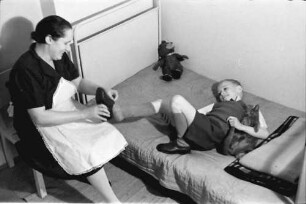 Bukarest: Familie Schmidt, Junge liegend [mit Haushälterin beim Schuhe anziehen]
