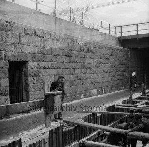 Pölitzer Weg: Bahnunterführung: Bau der Kanalisation: rechts Baustelle mit Arbeitern: links Fußgänger beim Blick in Baugrube: hinten rechts Frau