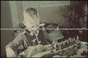 Junge mit Kriegsspielzeug vor dem Weihnachtsbaum