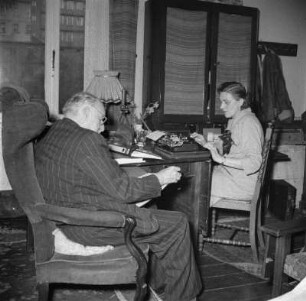 Der Maler Prof. Ernst Vollbehr (1876-1960) mit einer Mitarbeiterin? in seinem Atelier am Schreibtisch sitzend