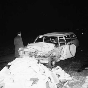 B 404: bei Tralau: Verkehrsunfall: Zusammenstoß von Pkw-Kombi mit Lkw: Pkw-Kombi mit eingedrückter Front: davor auf Fahrbahn zahlreiche Pakete von Ladung: links Polizist [Rückenansicht]: im Dunkeln, 12. Januar 1965